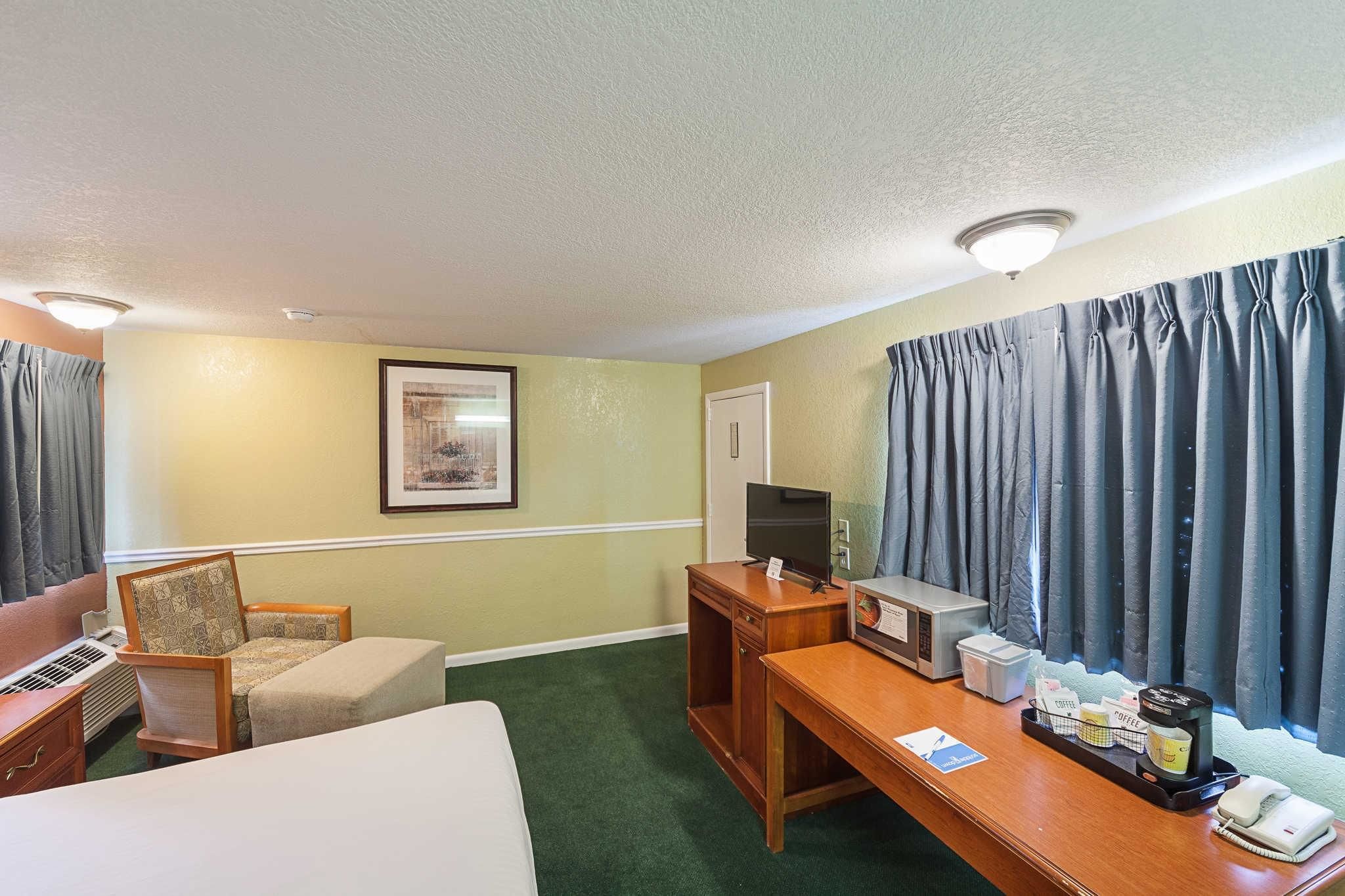 Une chambre d’hôtel avec un lit, une chaise, un bureau avec une machine à café, une télévision et des rideaux.