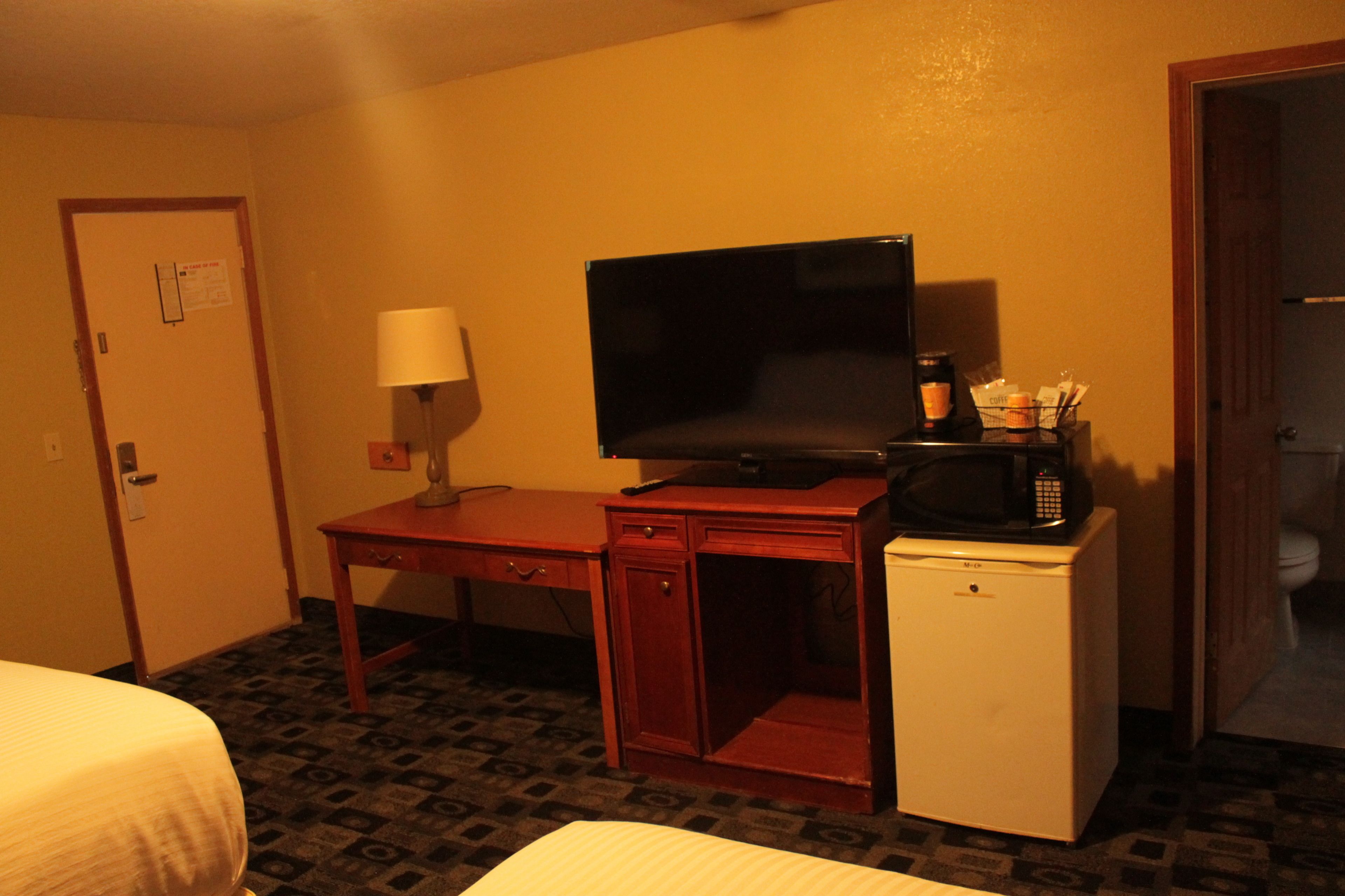 A hotel room with a bed, a desk with a television, a microwave, and a refrigerator.
