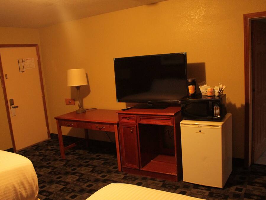 A hotel room with a bed, a desk with a television, a microwave, and a refrigerator.