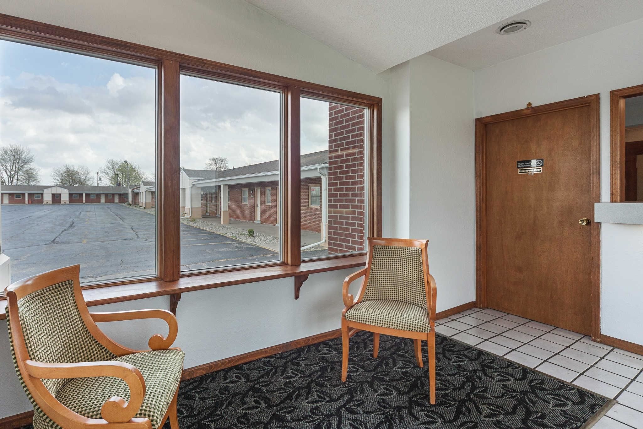 A hotel lobby with two wooden chairs, a large window, and a door with a sign.