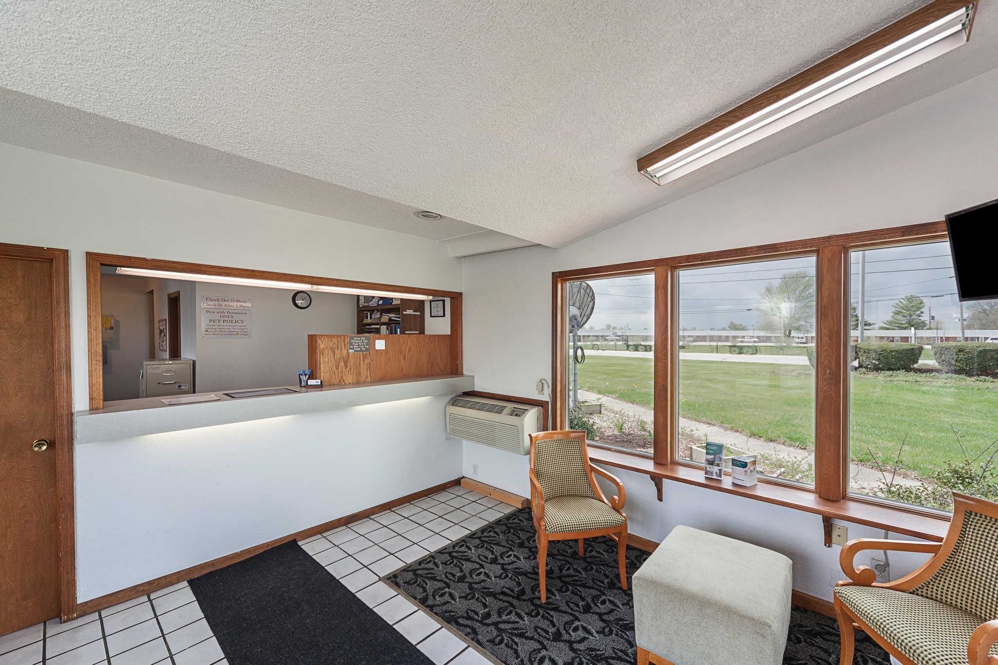 Een receptie met een receptiebalie, stoelen, een groot raam met uitzicht op de omgeving, en een luchtbeheersingsunit aan de muur.