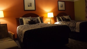 A hotel room with two beds, each with a headboard and a bedside lamp. There are framed pictures on the wall above the beds.