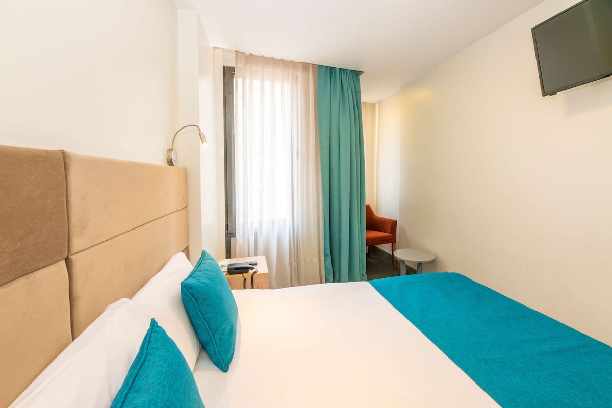 Habitación de hotel con una cama grande, un escritorio, una silla y un televisor en la pared.