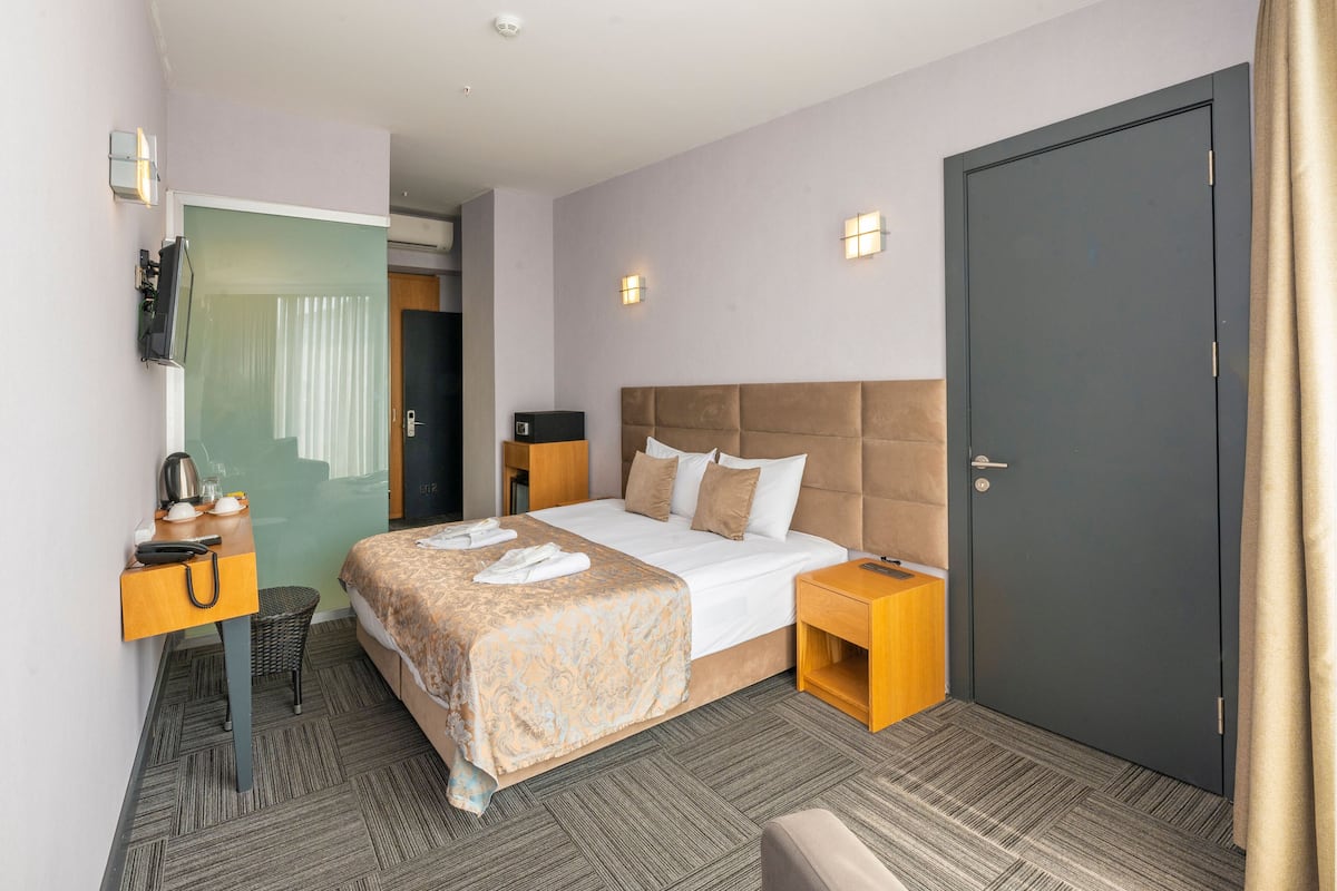 Una habitación de hotel con cama, mesita de noche, escritorio, silla y puerta.