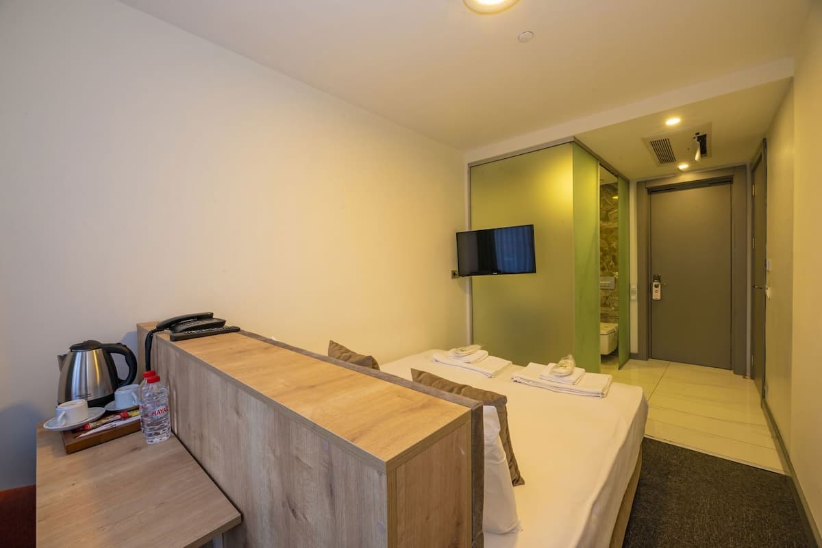 Habitación de hotel con un escritorio de madera, una cama con toallas, un televisor y un baño visible a través de una puerta.