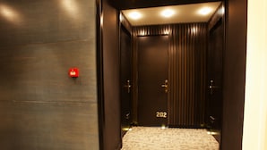 Um elevador moderno com interior escuro, um botão de emergência visível e o número 202 na porta.