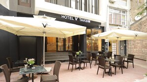 Uma área externa com mesas e cadeiras, guarda-sóis e uma placa indicando HOTEL V TAKSIM.