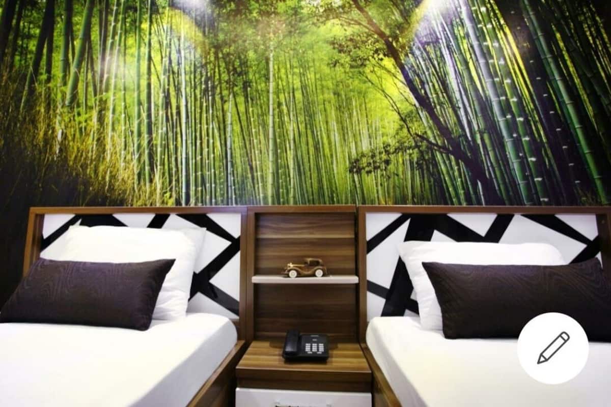 Une chambre d’hôtel avec deux lits, une table de chevet avec un téléphone et une fresque murale représentant une forêt de bambous.