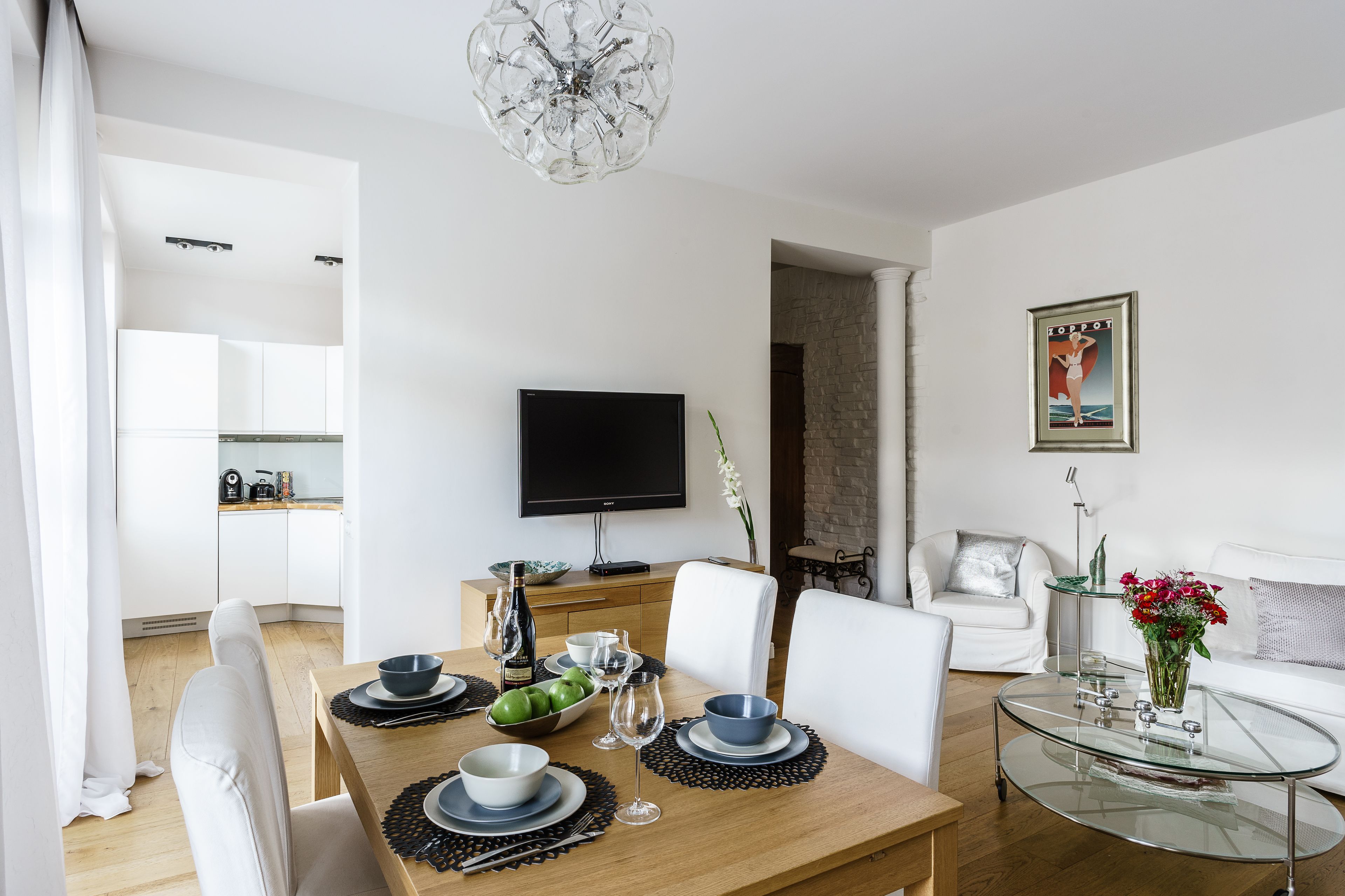 A modern living room with a dining area, a flat-screen TV, a glass coffee table, and a sofa.