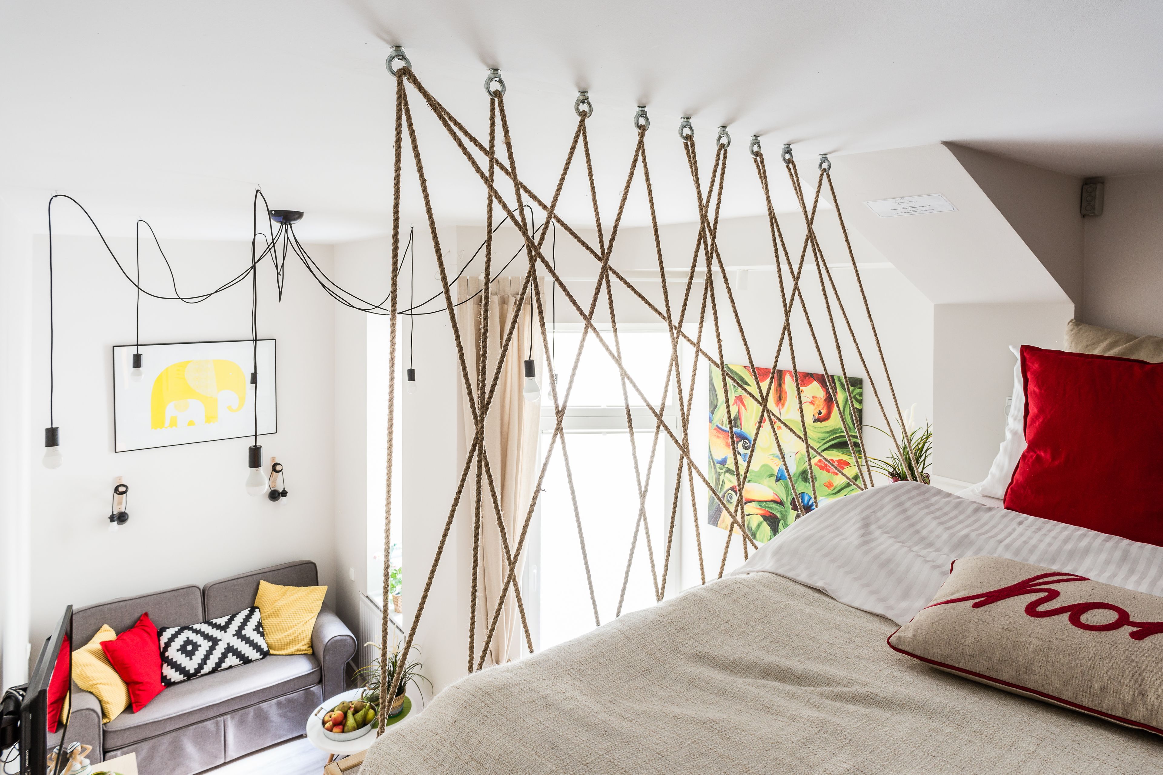A bedroom with a bed, a sofa, and a hanging rope decoration.