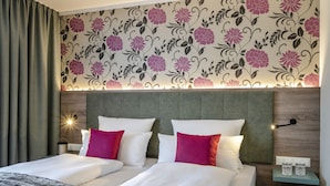 Una habitación de hotel con dos camas, un diseño de papel tapiz floral, un cabecero de madera y lámparas de noche.