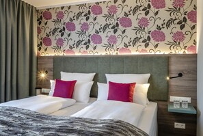 Una habitación de hotel con dos camas, un diseño de papel tapiz floral, un cabecero de madera y lámparas de noche.
