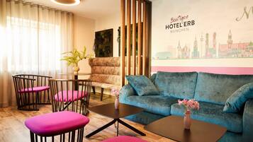 A modern hotel room with a blue sofa, pink chairs, a small table, and a cityscape mural.