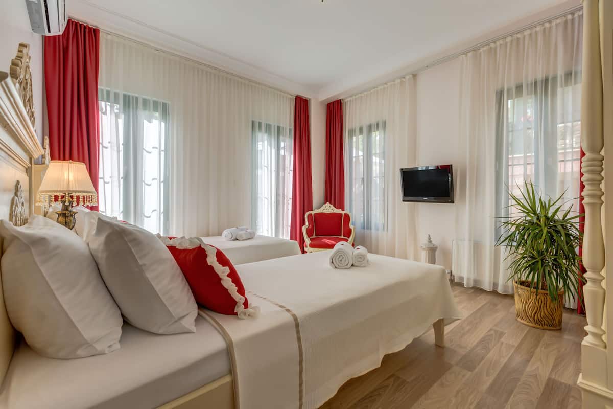 Habitación de hotel con dos camas, un televisor, una silla roja y una planta en maceta.