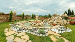 Un jardin avec un étang, des allées pavées de pierres et une statue.