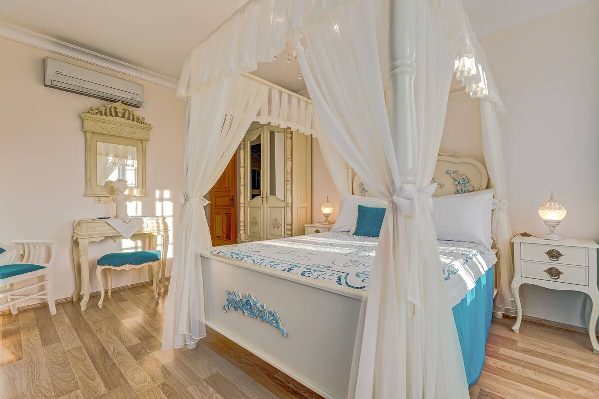 Un dormitorio con cama con dosel, tocador con espejo, escritorio y mesita de noche.