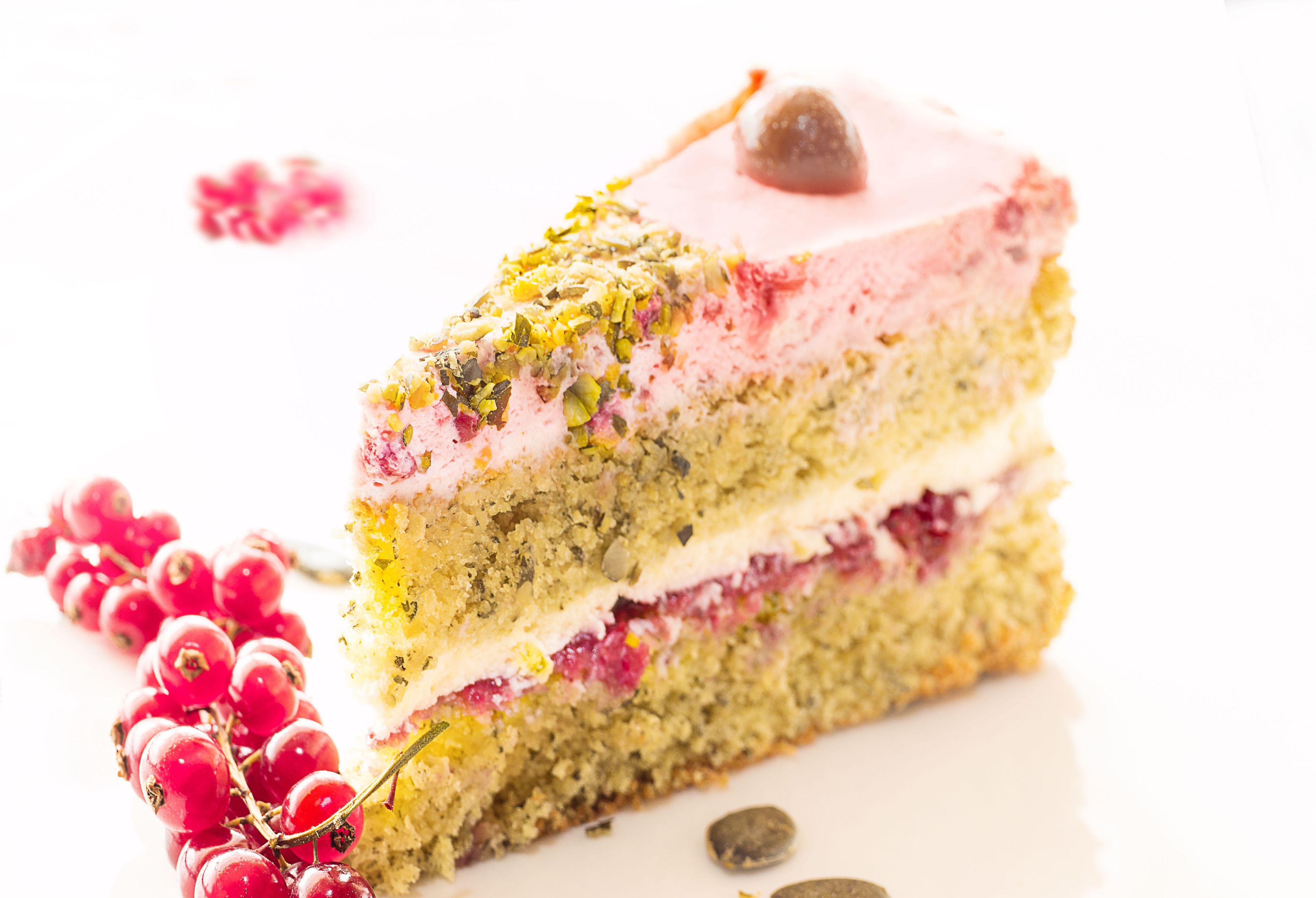 Una porción de pastel en capas con betún rosa y decoración de pistachos.