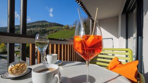 Una mesa con una copa de vino tinto, una taza de café y un cuenco de frutos secos en un balcón con vistas a un paisaje pintoresco.