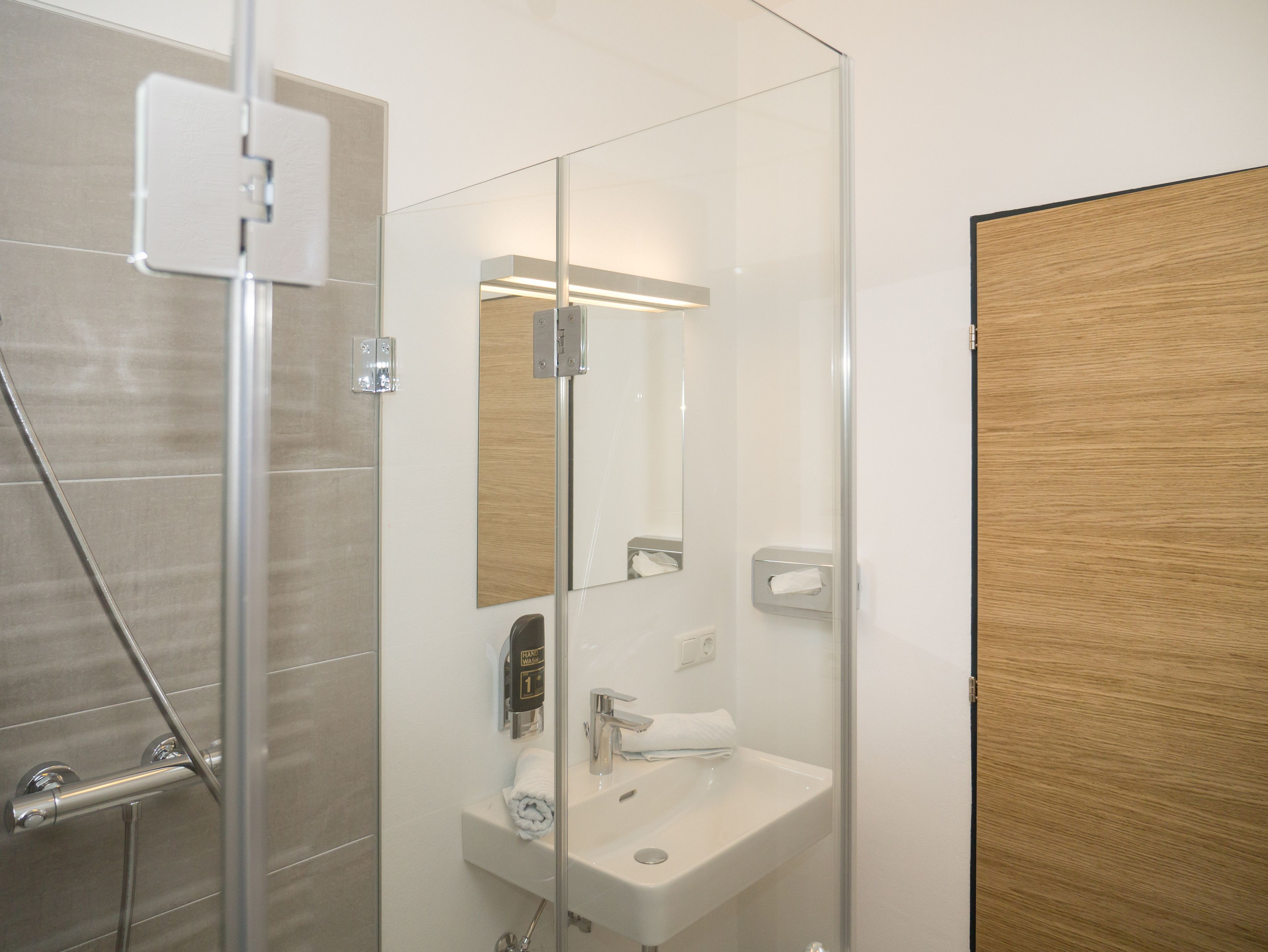 Une salle de bain moderne avec une douche à parois de verre, un lavabo blanc et une porte en bois.