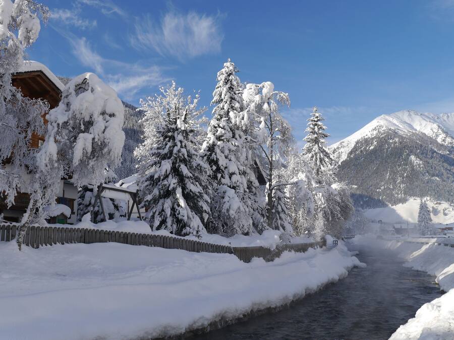 Paisaje nevado con una cabaña de madera, un río y árboles cubiertos de nieve.