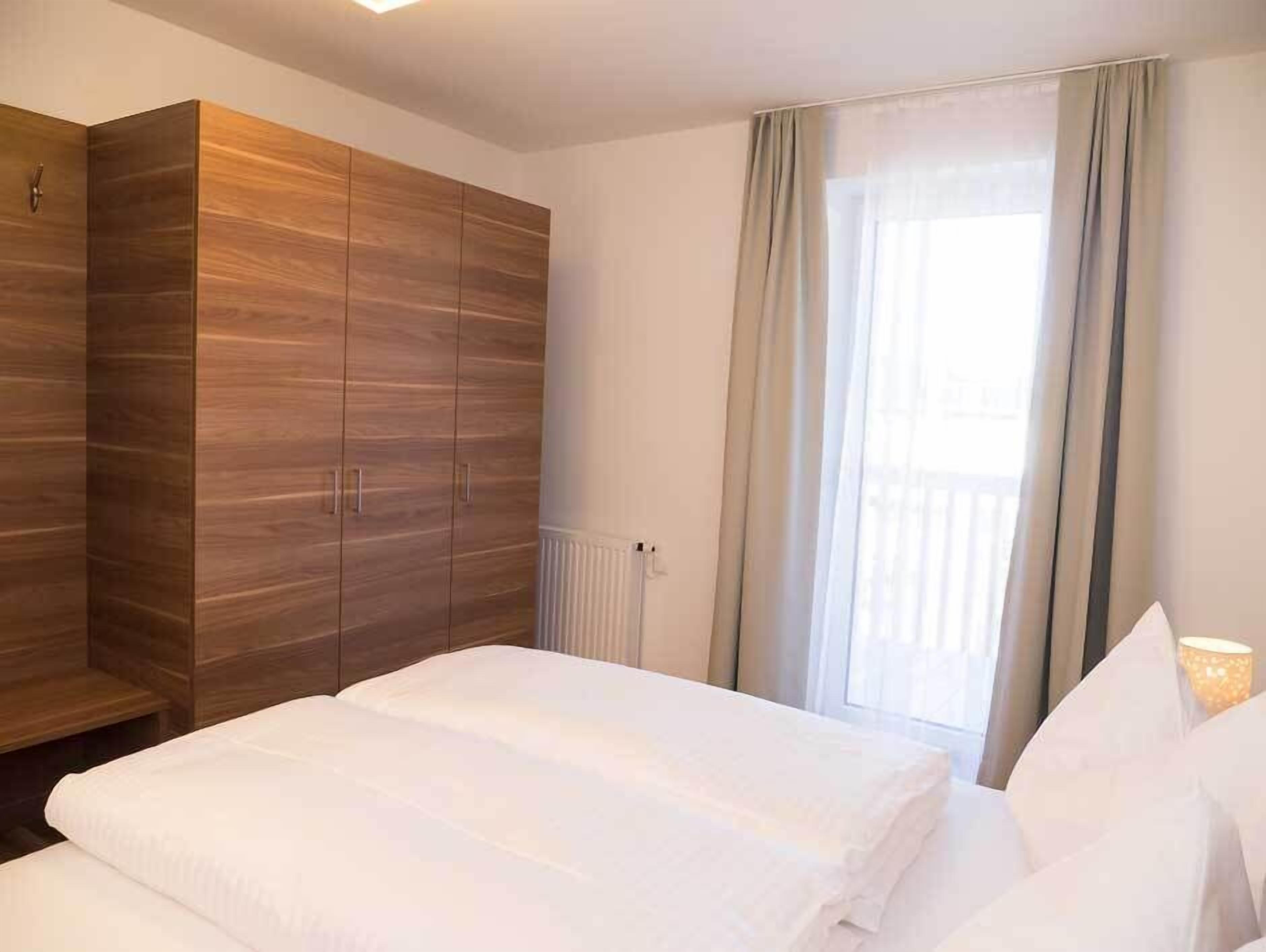 Habitación de hotel con un armario grande, una cama con ropa blanca y un ventanal con cortinas.