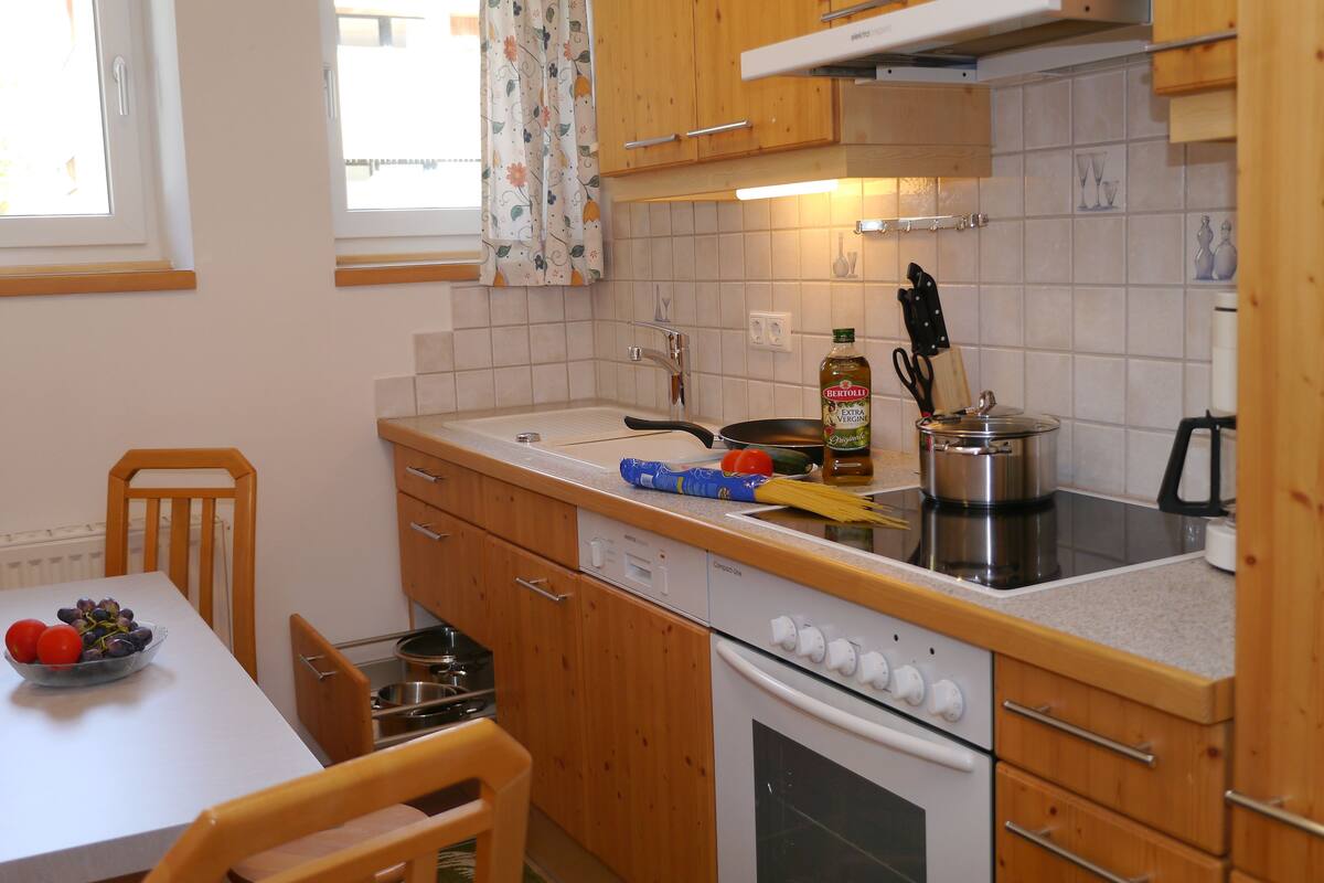 Una cocina con armarios de madera, encimera blanca, estufa y una mesa de comedor con sillas.