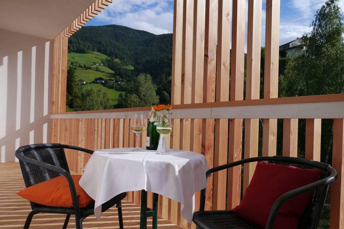 Una terraza de madera con una mesa, sillas, una botella de vino y una copa.