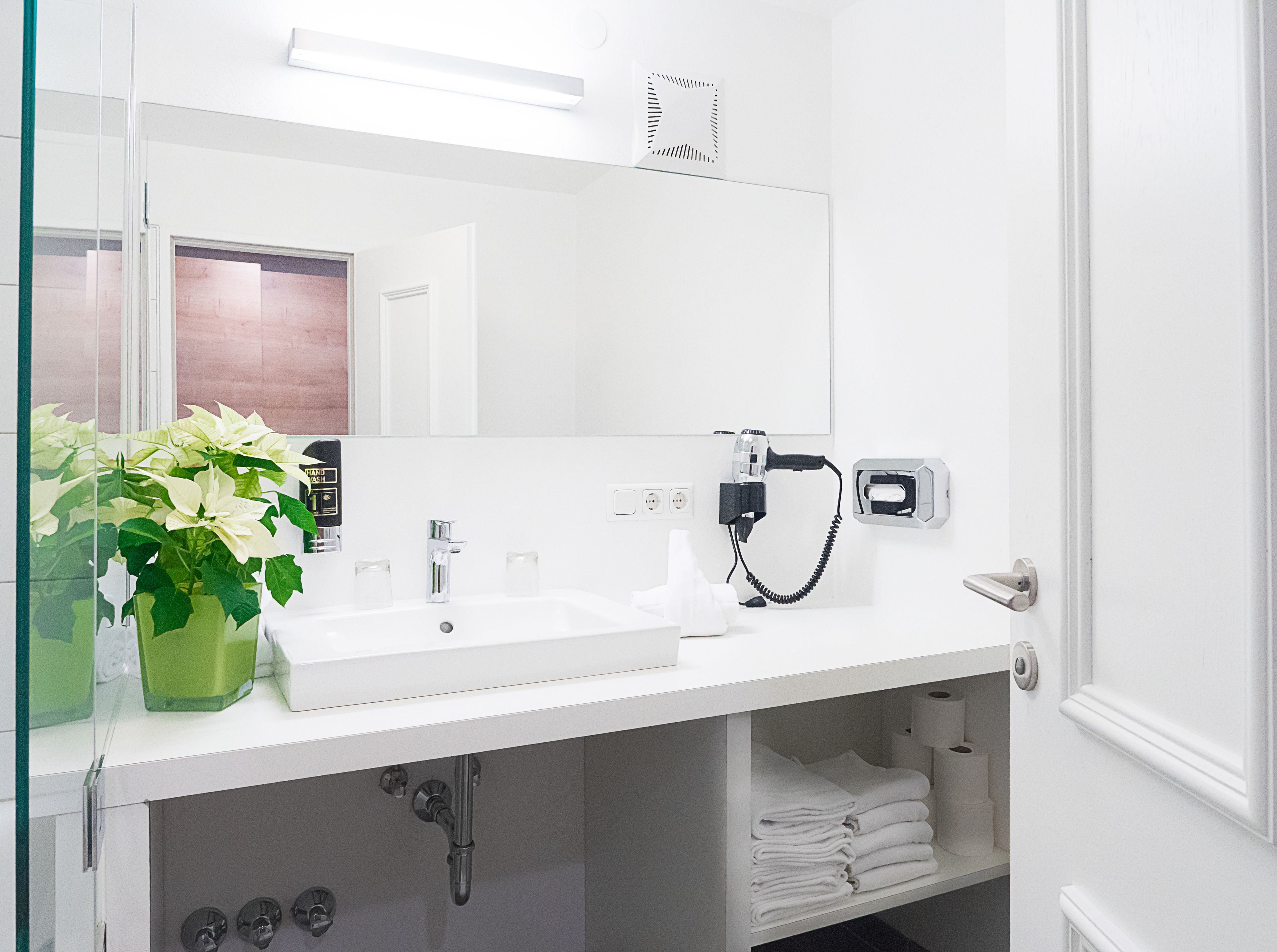 A modern bathroom with a white sink, a mirror, a hairdryer, and a towel rack.