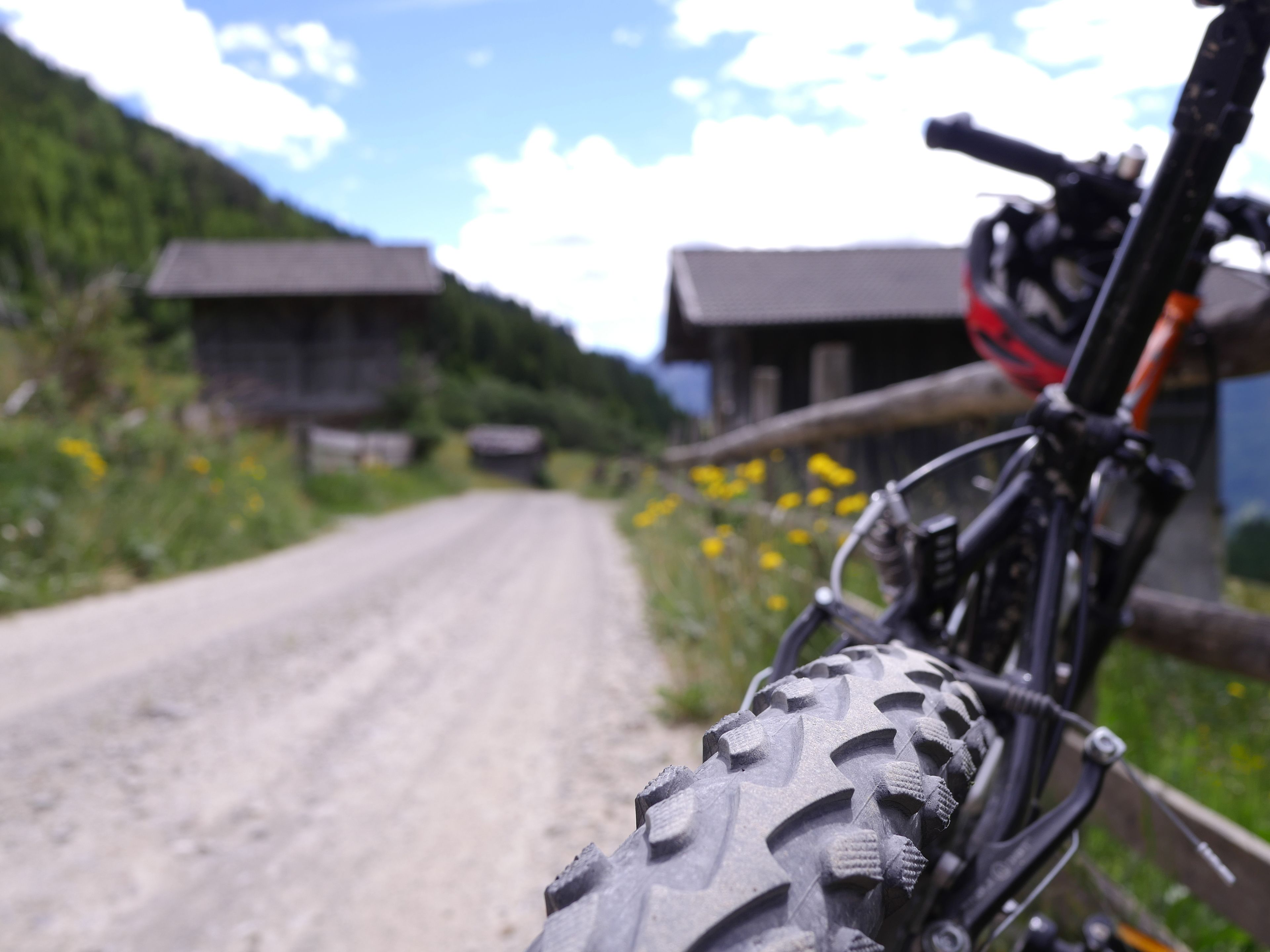 Primer plano de la llanta de una bicicleta de montaña en un camino de tierra con casas al fondo.