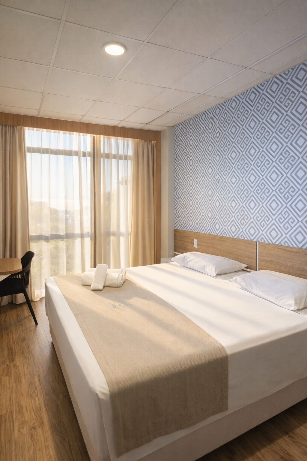 A hotel room with a large bed, a desk, and a window with curtains.