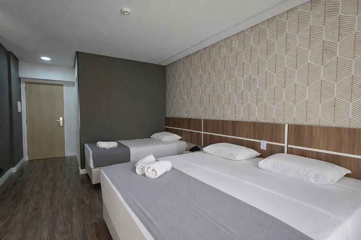 Een hotelkamer met twee bedden, een houten hoofdeinde, een behang met patroon en een deur.