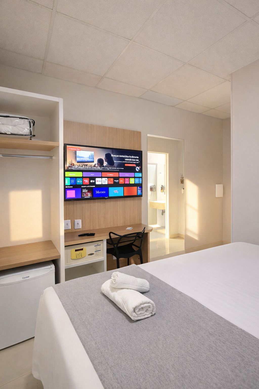 Una habitación de hotel con cama, escritorio con computadora, televisor y armario.