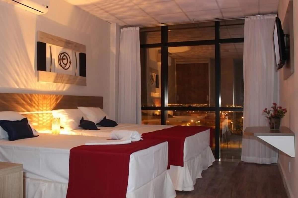 Hotelkamer met een groot bed, een klein tafeltje, een televisie en uitzicht op de stad door grote ramen.