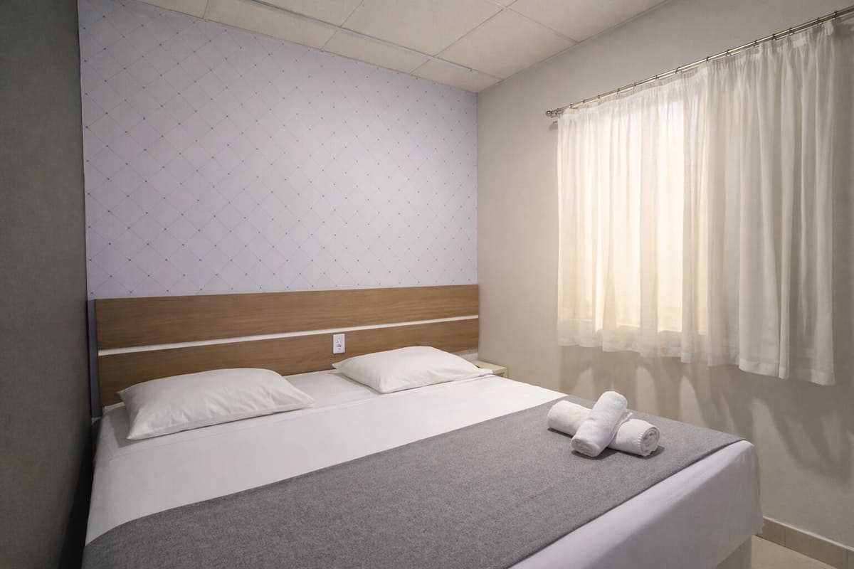 Een netjes opgemaakt bed met een grijze deken, witte kussens en een houten hoofdbord.