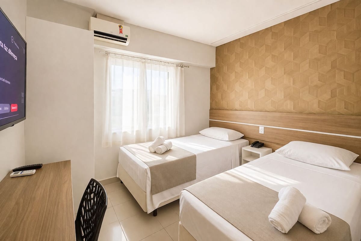 Een hotelkamer met twee bedden, een televisie, een airconditioner en een houten hoofdeinde.