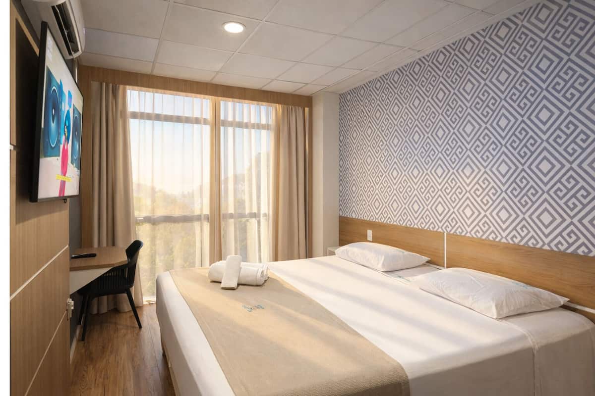 Een hotelkamer met een bed, een bureau, een stoel, een televisie en een behang met een patroon.
