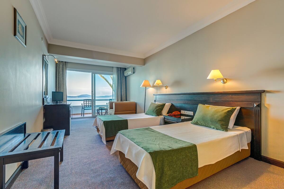 A hotel room with two beds, a desk, a chair, and a TV.
