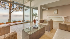 Een moderne woonkamer met rieten meubels, een glazen salontafel en uitzicht op zee door grote ramen.