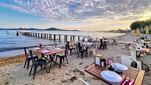Een restaurant aan het strand met terras, houten vlonder en uitzicht op zee en bergen.