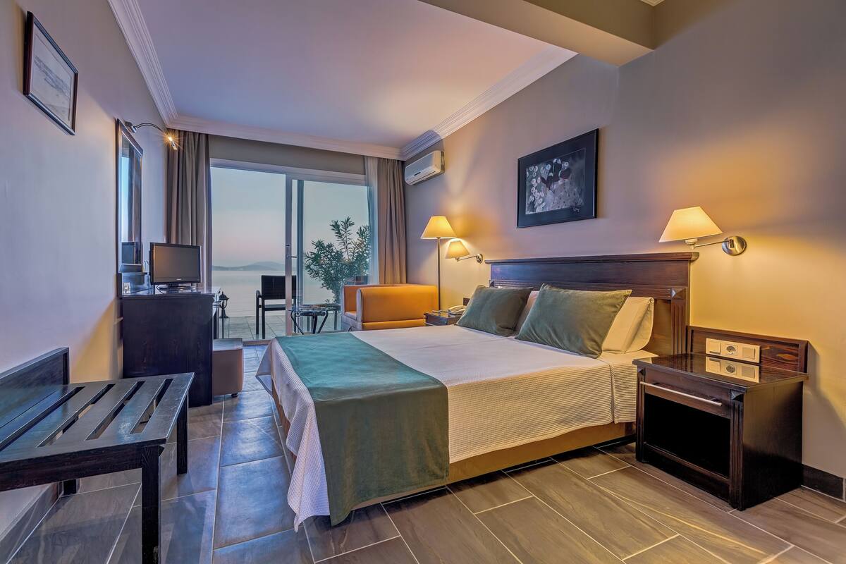 A hotel room with a large bed, bedside tables, a desk, a chair, and a view of the outdoors.
