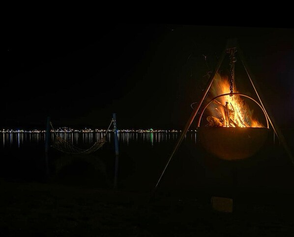 A campfire at night with a metal structure, a rope, and a metal railing in the background.