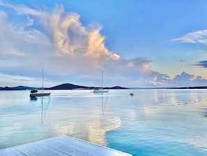 A calm body of water with two sailboats and a dock in the foreground. - Cunda Oteli (Ayvalik)