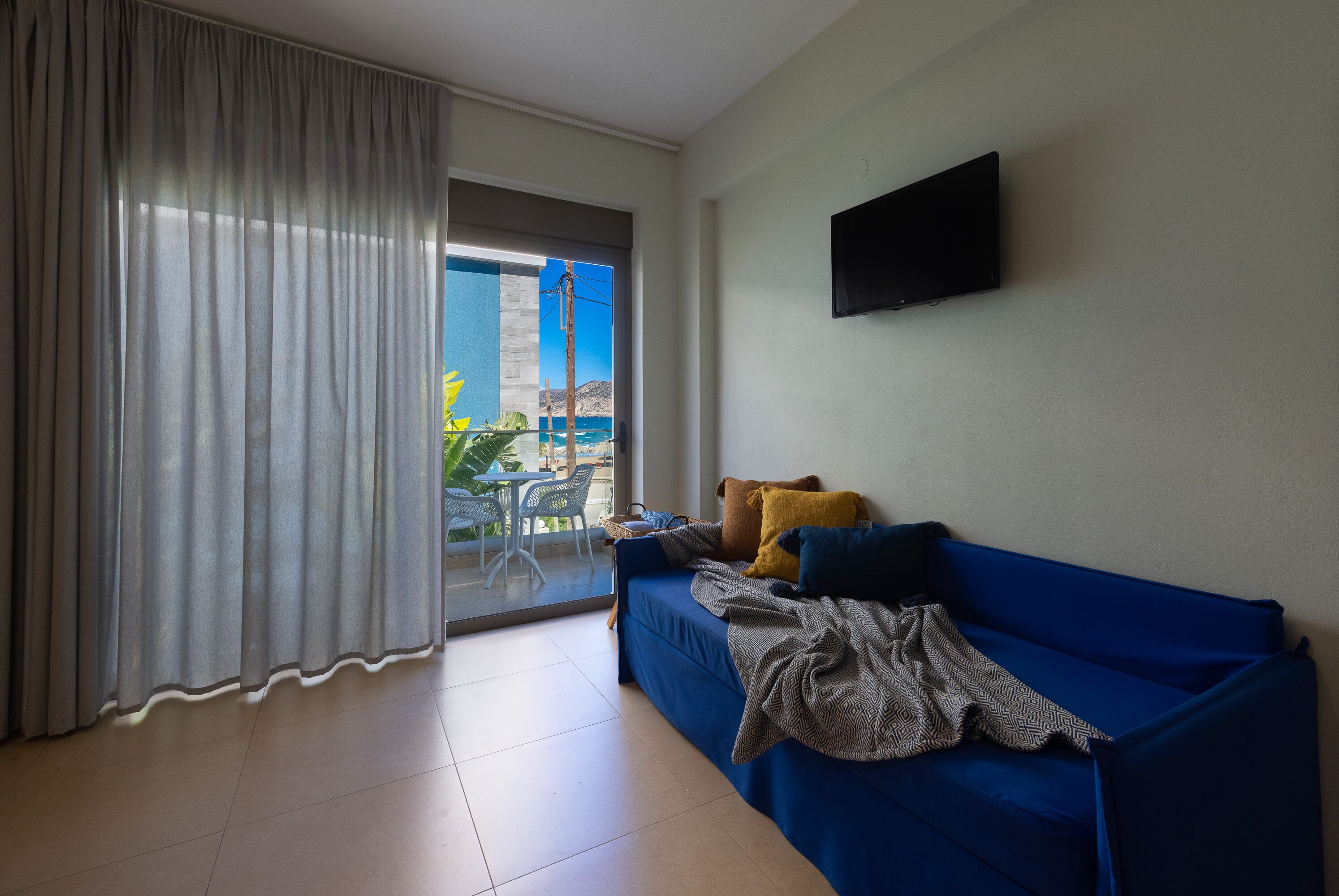 Una habitación con un sofá azul, un televisor instalado en la pared y vistas al exterior a través de un ventanal.