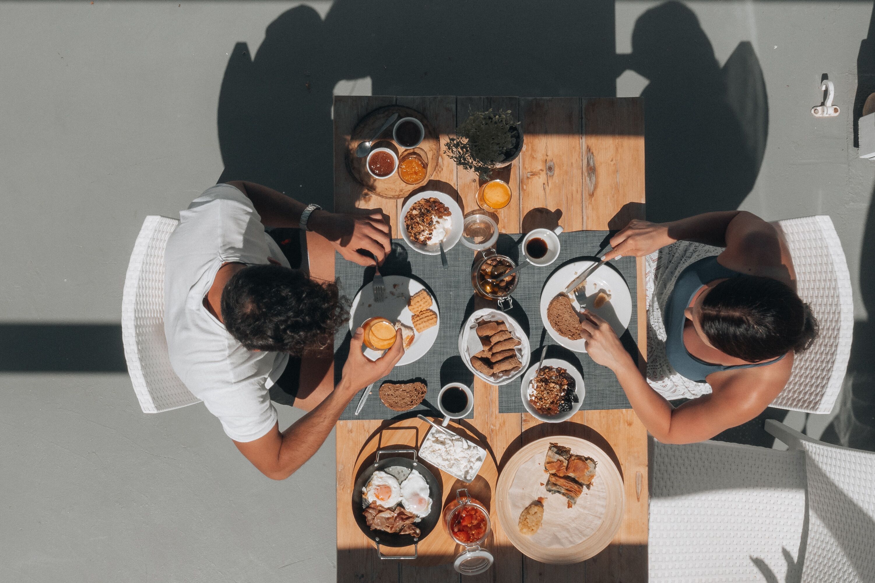 Vista cenital de una mesa de comedor con diversos alimentos para el desayuno, como huevos, tostadas y bebidas.