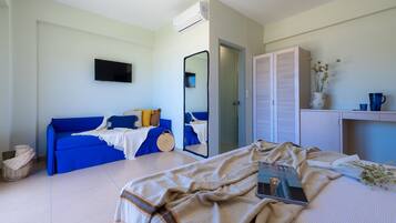 Un dormitorio moderno con un sofá azul, una cama con una manta color beige, una mesita de noche con un libro y un espejo.