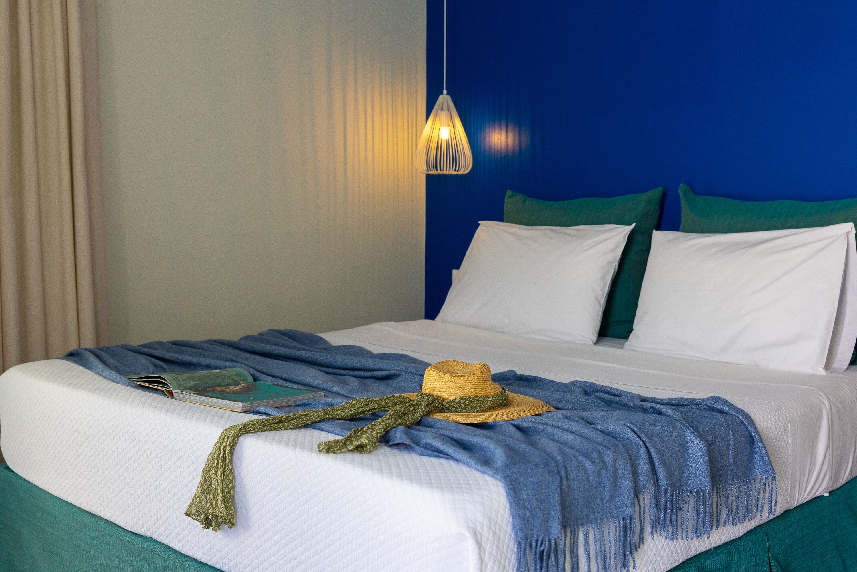 A neatly made bed with a hat, a book, and a blanket.