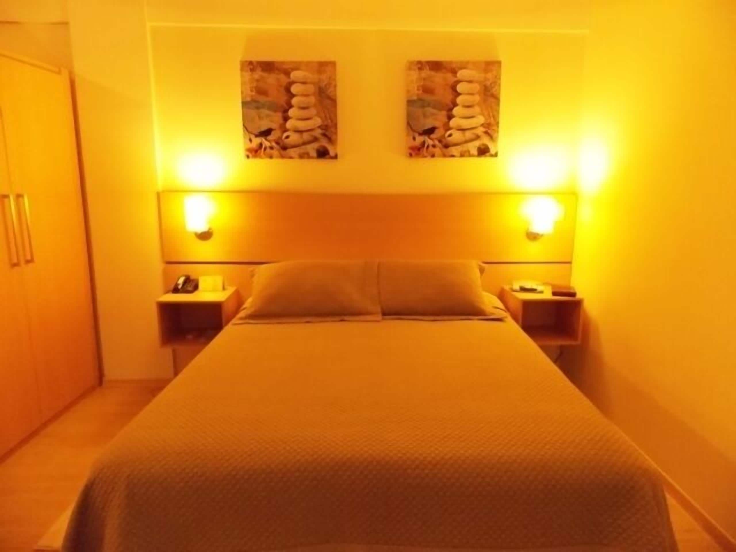 A hotel room with a bed, two bedside tables, a nightstand, and a wardrobe.