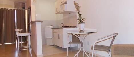 Una cocina moderna con armarios blancos, un refrigerador blanco y una zona de comedor con una mesa de vidrio redonda y dos sillas.