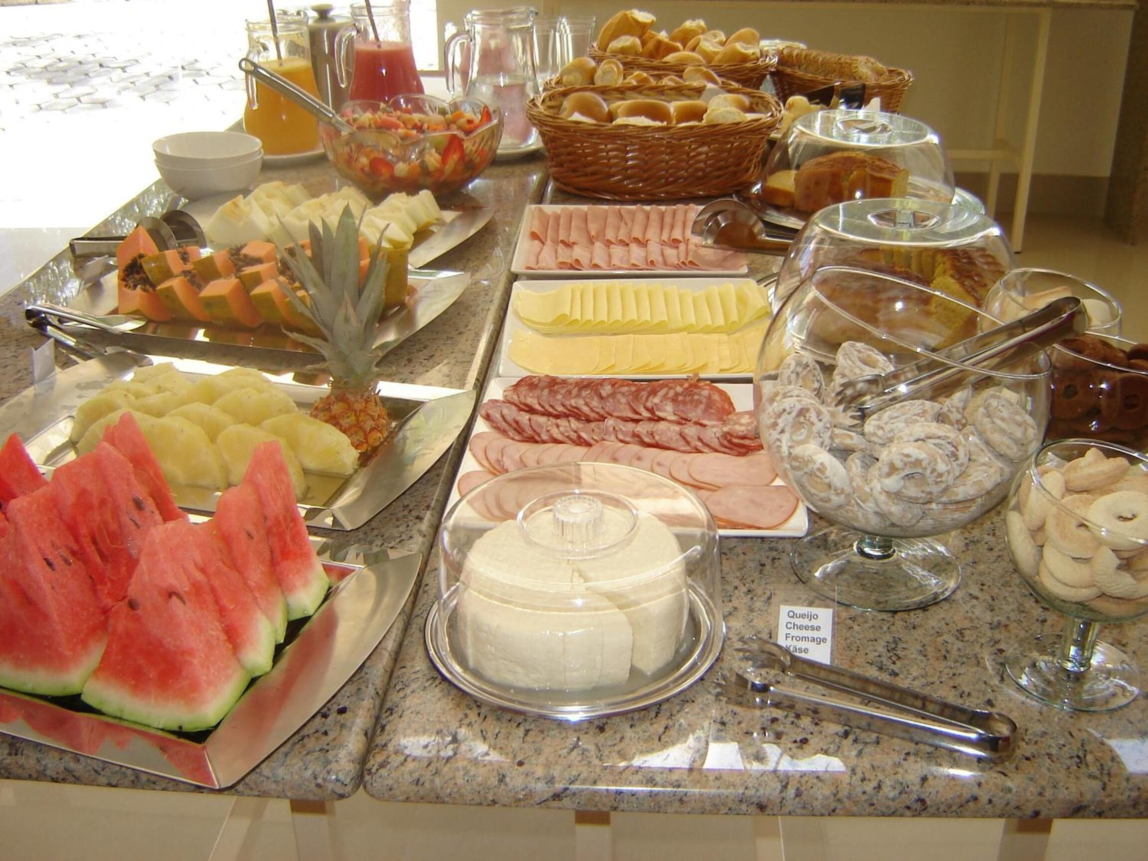 Un bufé con diversas opciones de comida, incluyendo frutas, quesos, carnes y pastelería.