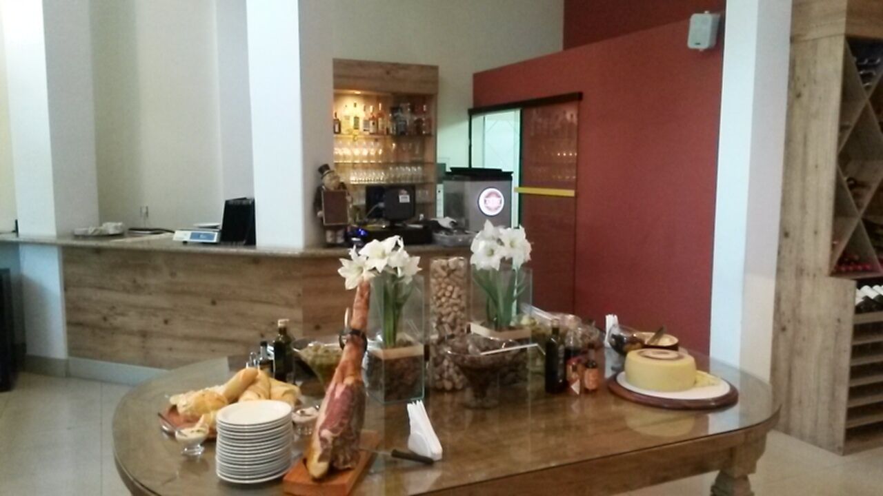 Un comedor con una mesa de madera dispuesta para una comida, incluyendo platos, cubiertos y un pastel. Se ve una barra al fondo, con botellas y vasos.